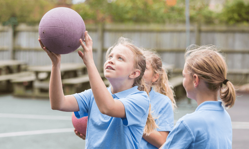 3 young girls playing netball in school uniform