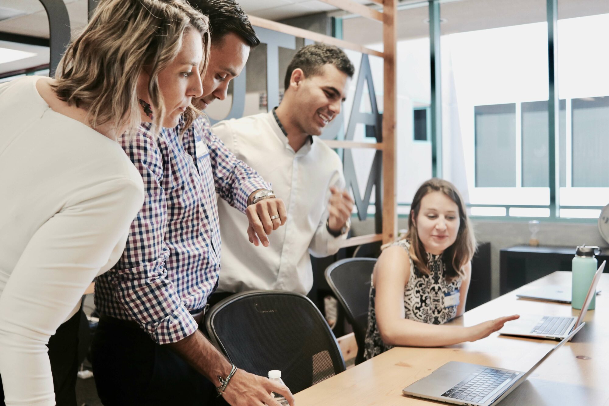 4 young professionals working together at an office over a laptop, smiling and collaborating