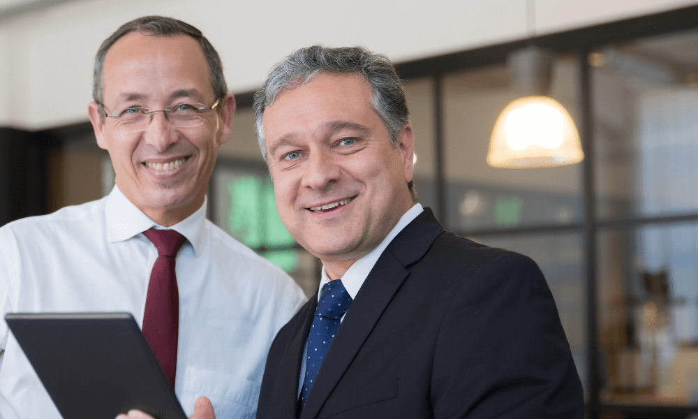 two older greying men smiling in suits