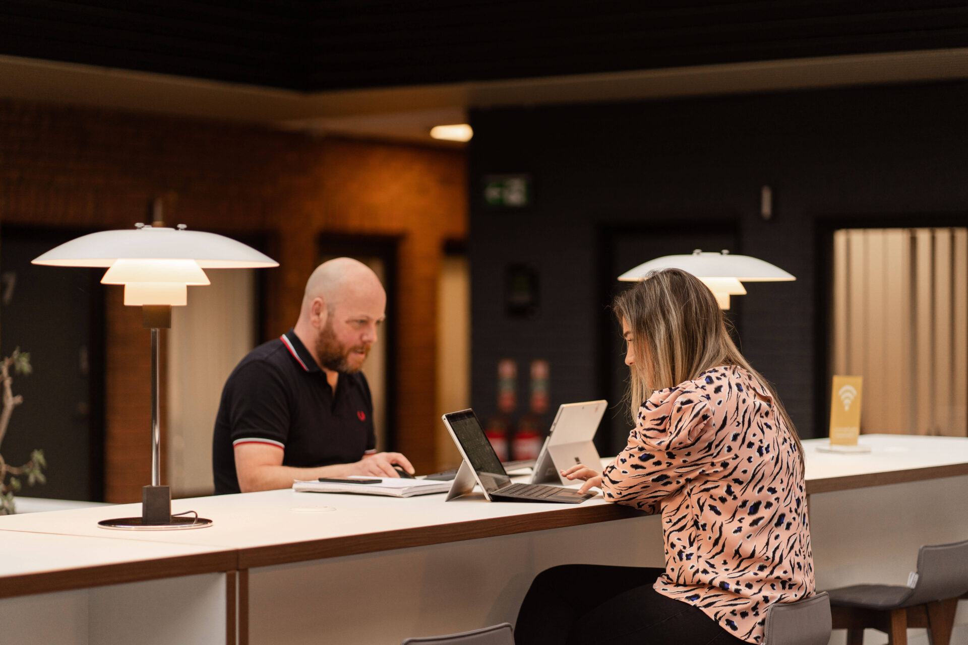 Two pertemps workers working on laptops in a communal space in the warrington office area