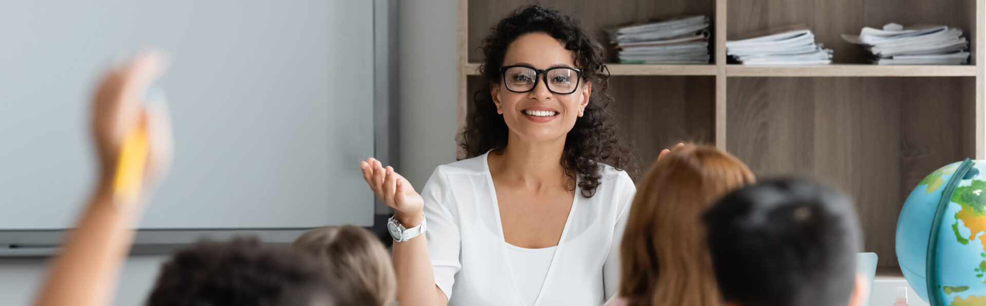 A young woman teacher with brown curly hair and glasses looks at her smiling