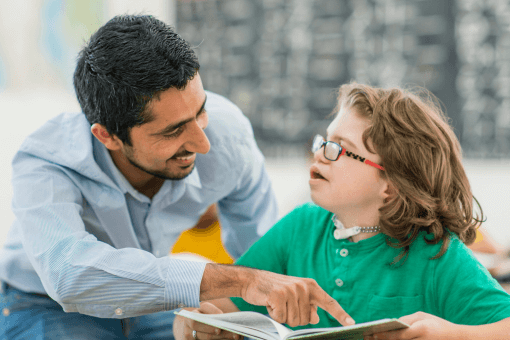 A male teacher helping a student with SEND whilst smiling