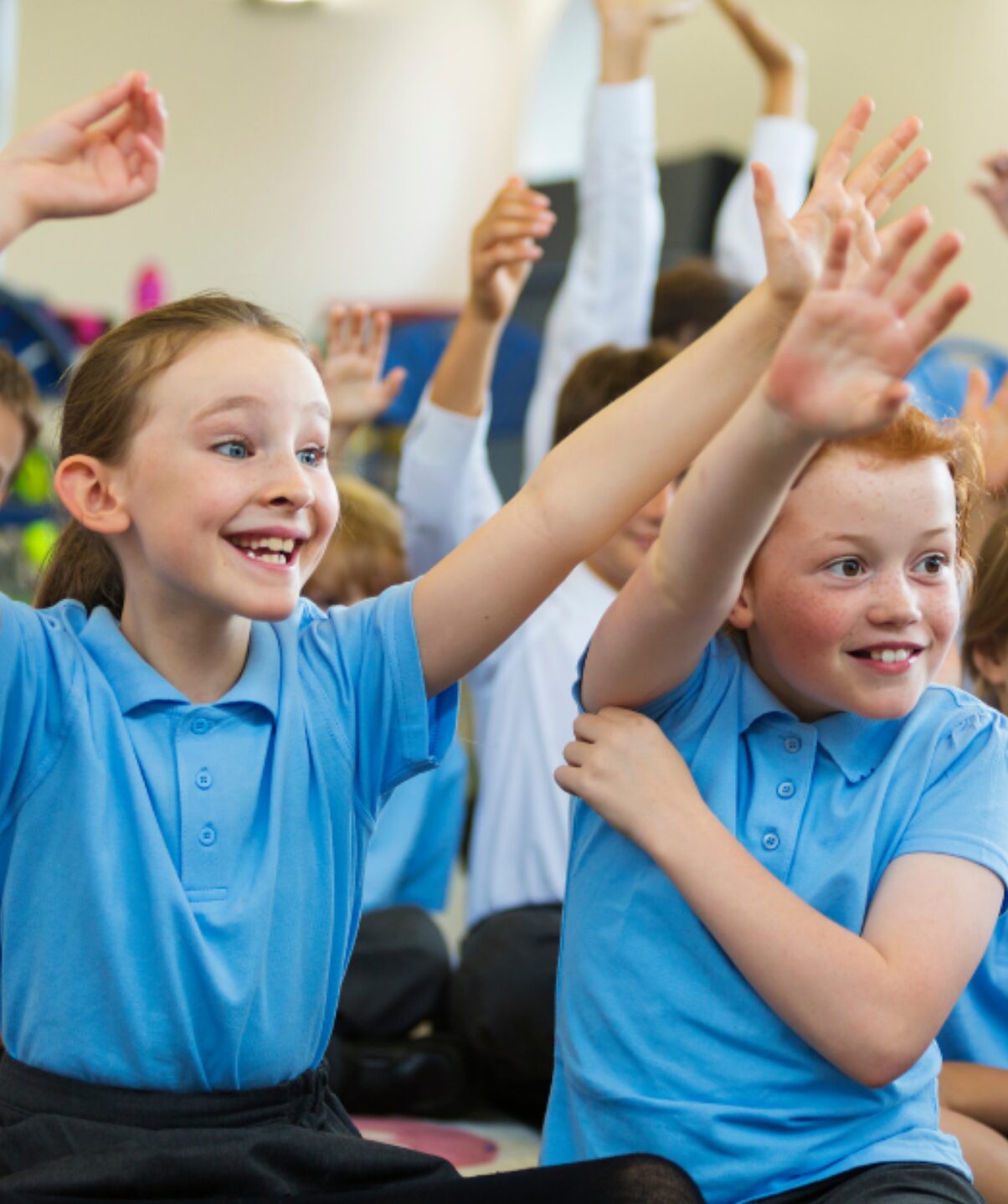 young primary school children in blue uniform looking excited and puting their hands up