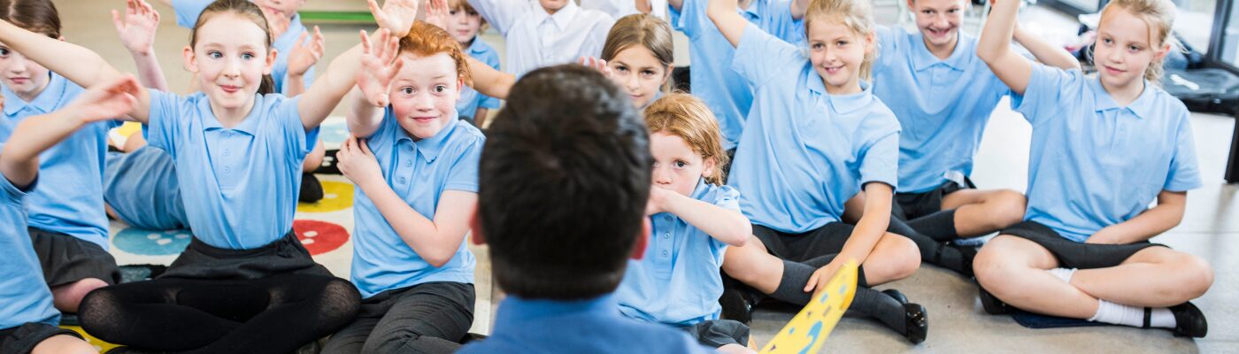 The back of the teacher's head is out of focus and there are teachers with their hands high